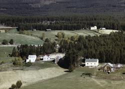 Flyfoto,skog og jordbrukslandskap med gårsdbruk. Nevnt som J