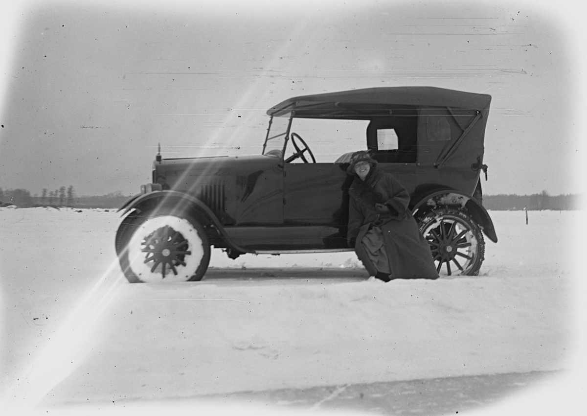 En kvinna vid en bil.
Hjälmaren den 17 februari. 
Bilen på bilden är en Gray Touring från 1922. Den ser ut att vara ny vid fototillfället eftersom den har en temporär registreringsskylt (interimsskylt).