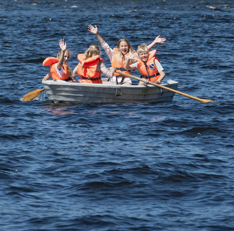 Bildet viser barn som er ute i båt på glomma. De vinker til fotografen.