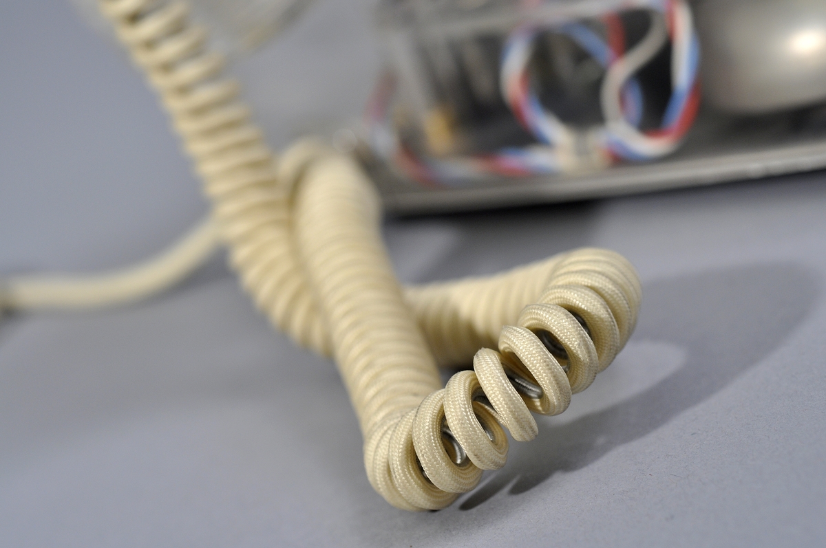 Telefonapparat BC 560, ändstationsapparat för AT-system. Bordstelefon modell m50 av genomskinlig termoplast med apparatsnöre anslutet till väggplint med transparent plastlock.