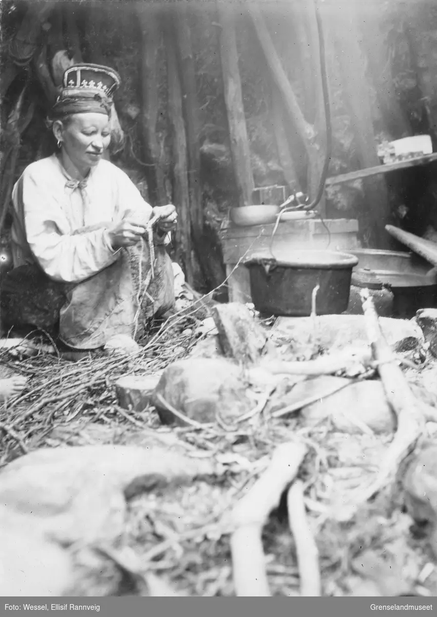 Skoltesamekvinnen Tatjana Fesdolova Titoff inne i gammen ved laksefiskeplassen ca 1900. Hun strikker.