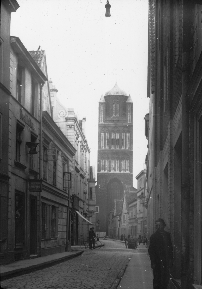Skioptikonbild med motiv från gata i Stralsund med kyrkan St. Jakobi Kirche i bakgrunden.
Bilden har förvarats i kartong märkt: Resan 1912. Stralsund. 9. Text på bild: "Jacobikirche".