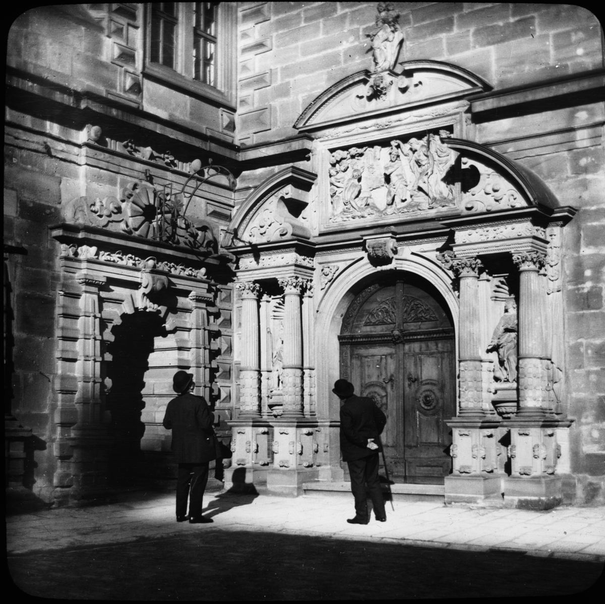 Skioptikonbild med motiv av två män vid porten till slottet Johannisburg i Aschaffenburg.
Bilden har förvarats i kartong märkt: Resan 1908. Aschaffenburg 7. XXVIII.
