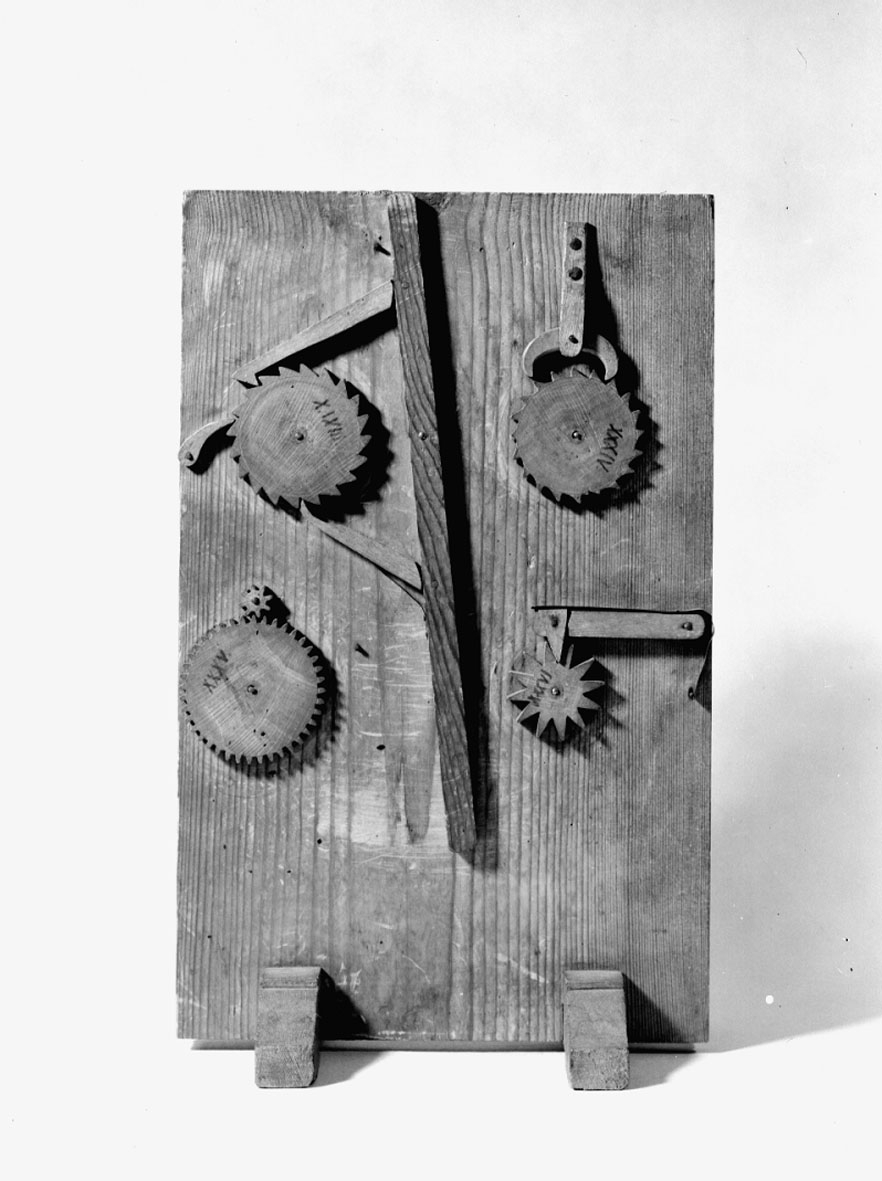 Modell ur Polhems mekaniska alfabet. Text på föremålet: XXXIII, XXXIV, XXXV, XXXVI. Den övre vänstra mekanismen visar hur en pendelrörelse hos den långa armen överförs till en roterande rörelse hos spärrhjulet. Den övre högra mekanismen visar hur ett oro överför rörelsen hos en pendel på tavlans baksida till en roterande rörelse hos spärrhjulet. Nedre vänstra mekanismen visar en kugghjulsutväxling och den nedre högra ett spärrhjul med fjäderbelastad spärr.