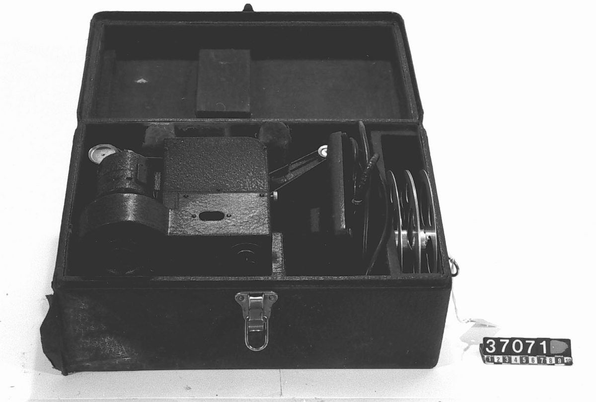Smalfilmsprojektor för 16 mm film, 100-125 V, 850 W. 2 tums kodak-lins med snäckgångsinställning. Steglös variabel hastighet. Monteras på gjutjärnsfot. Motstånd: TM 37.072. Transformator: TM 37.070. Märke: Kodascope, modell EE.
Tillbehör: 2 tomspolar, anslutningskabel och svart originalväska med bärhandtag.
