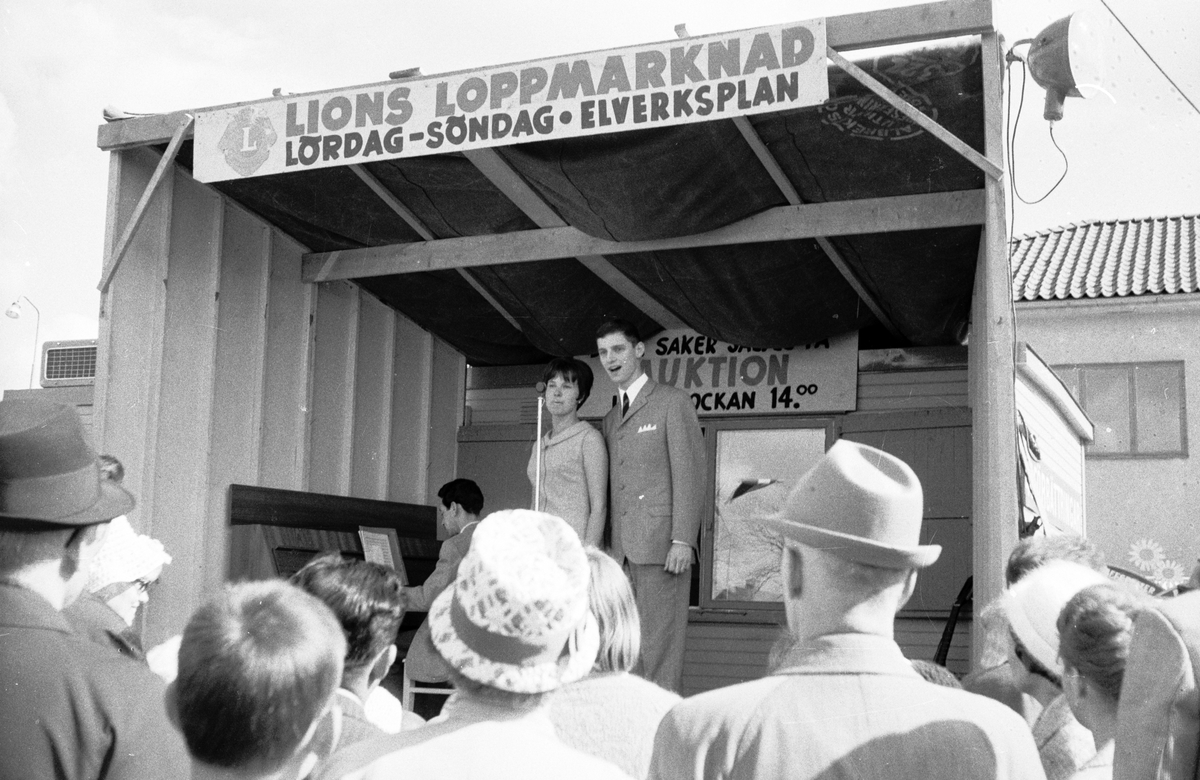 Lions, en ideell internationell välgörenhetsorganisation, har loppmarknad på Elverksplan i Huskvarna. På en liten scen uppträder Ellen Pelmas och Hans Josefsson, vid pianot sitter Arne Siwerth.