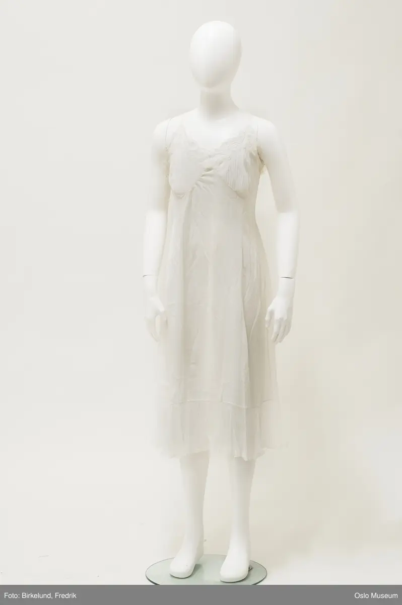 Utfyllende opplysninger:
A: Benklær. Livet med strikk. Utskrådd, meget vide, skråklippet ved nedkanten, her besetning av bred, "plissert" tyllkant med tunget blonde.

B: Underkjole. Skulderstropper. Bysten med dekor som A, nedkanten det samme.