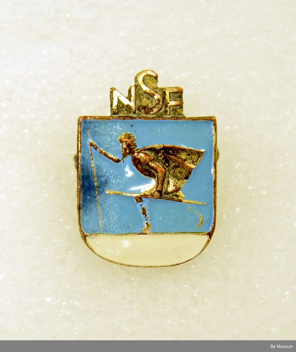 Pin - med innskrift):
"NSF" (Norges Skiforbund)
I metall og emalje.
Med nål bak.