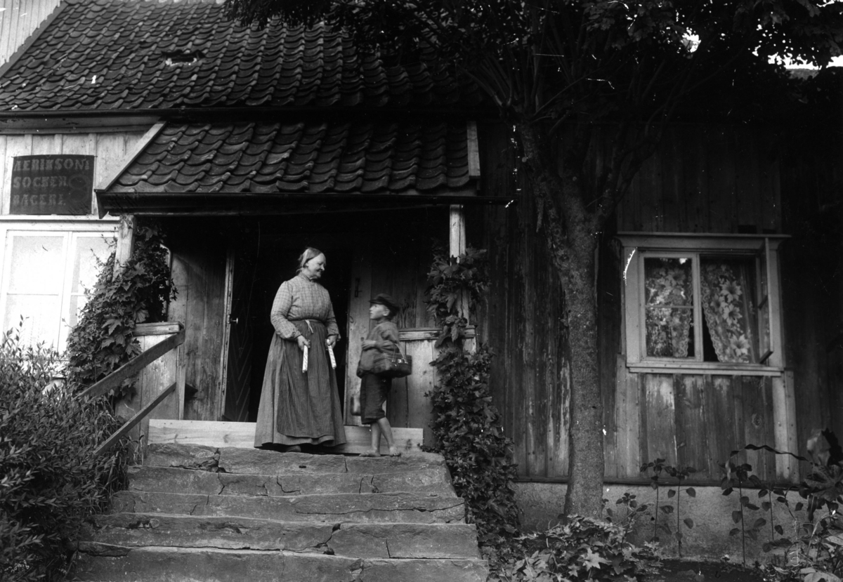 Polkagrisbagaren Amalia Erikson och pojken Gustaf Hellberg på trappan till sitt hus.