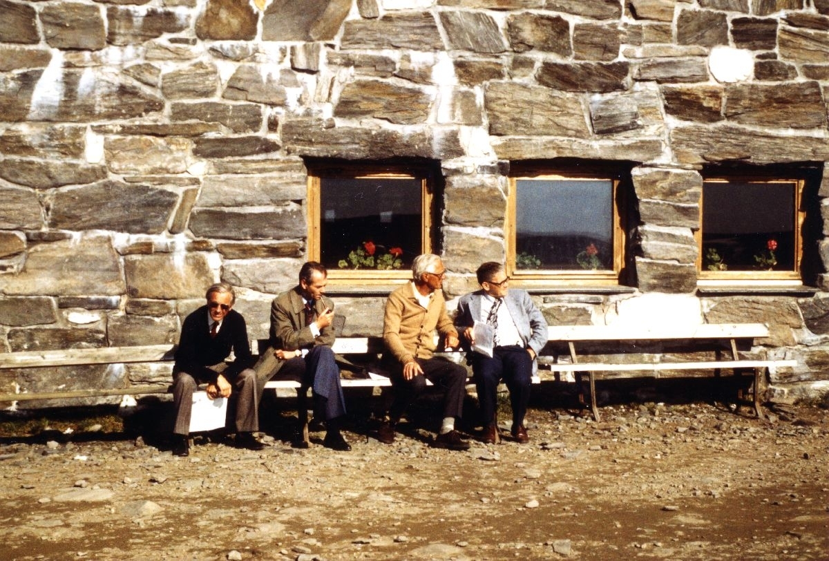 Landskap. Nordkapp. Utenfor Nordkapphallen sitter 4 personer og slapper av i solskinnet.