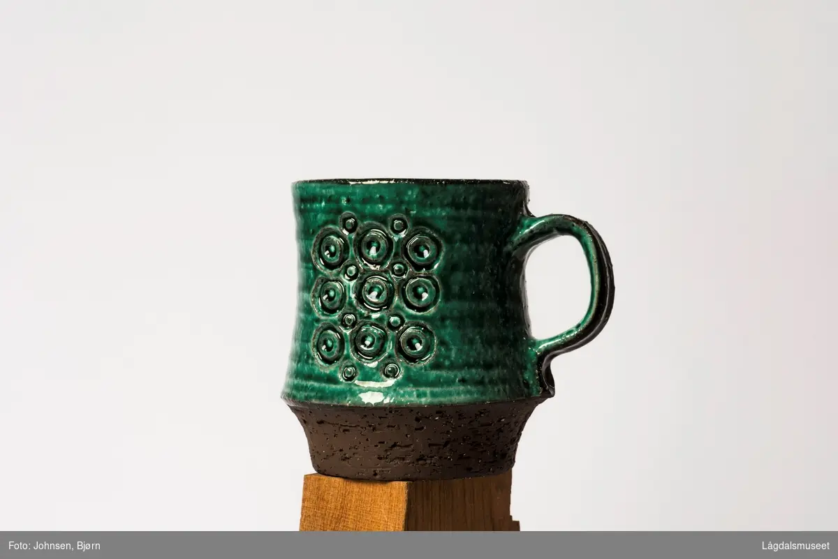 Stor kopp dekorert med grønn begitning og sirkler i front.
