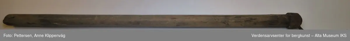 Et langt treskaft med kurvet jernpigg i den ene enden, festet med jernring. Jernpiggen er delvis felt inn i treskaftet.