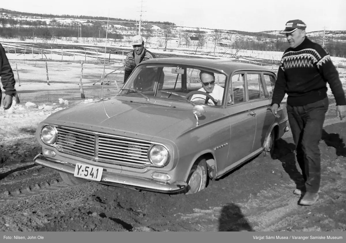 Bil som har kjørt seg fast i Bunes, sjåføren sitter inne i bilen og tre andre personer står og går på veien utenfor. Bildet er tatt våren 1967.