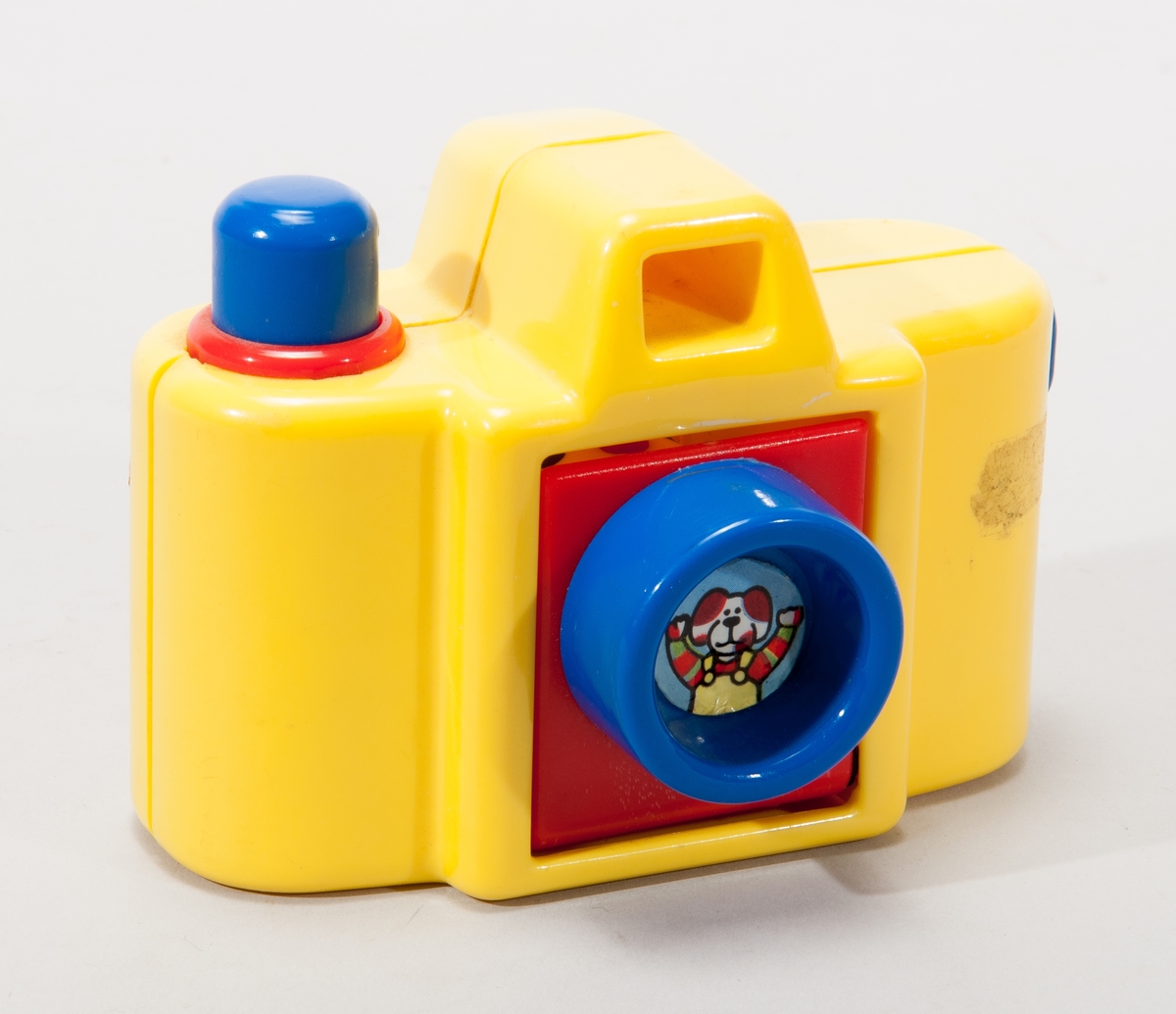 Leksakskamera i gul plast, linsen fälls ner när man trycker på utlösaren och ett clownhuvud visas då.