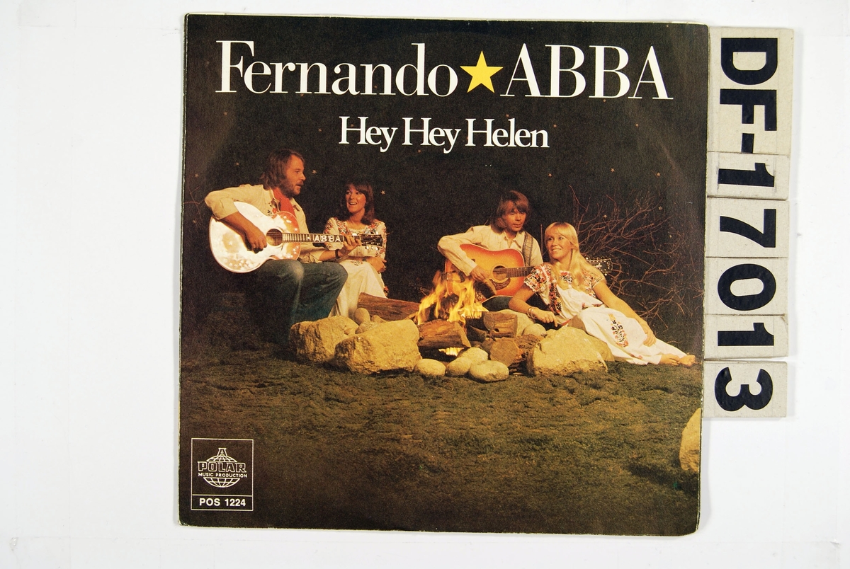 Fotografi av de fire medlemmene i ABBA sittende med gitarer rundt et bål.