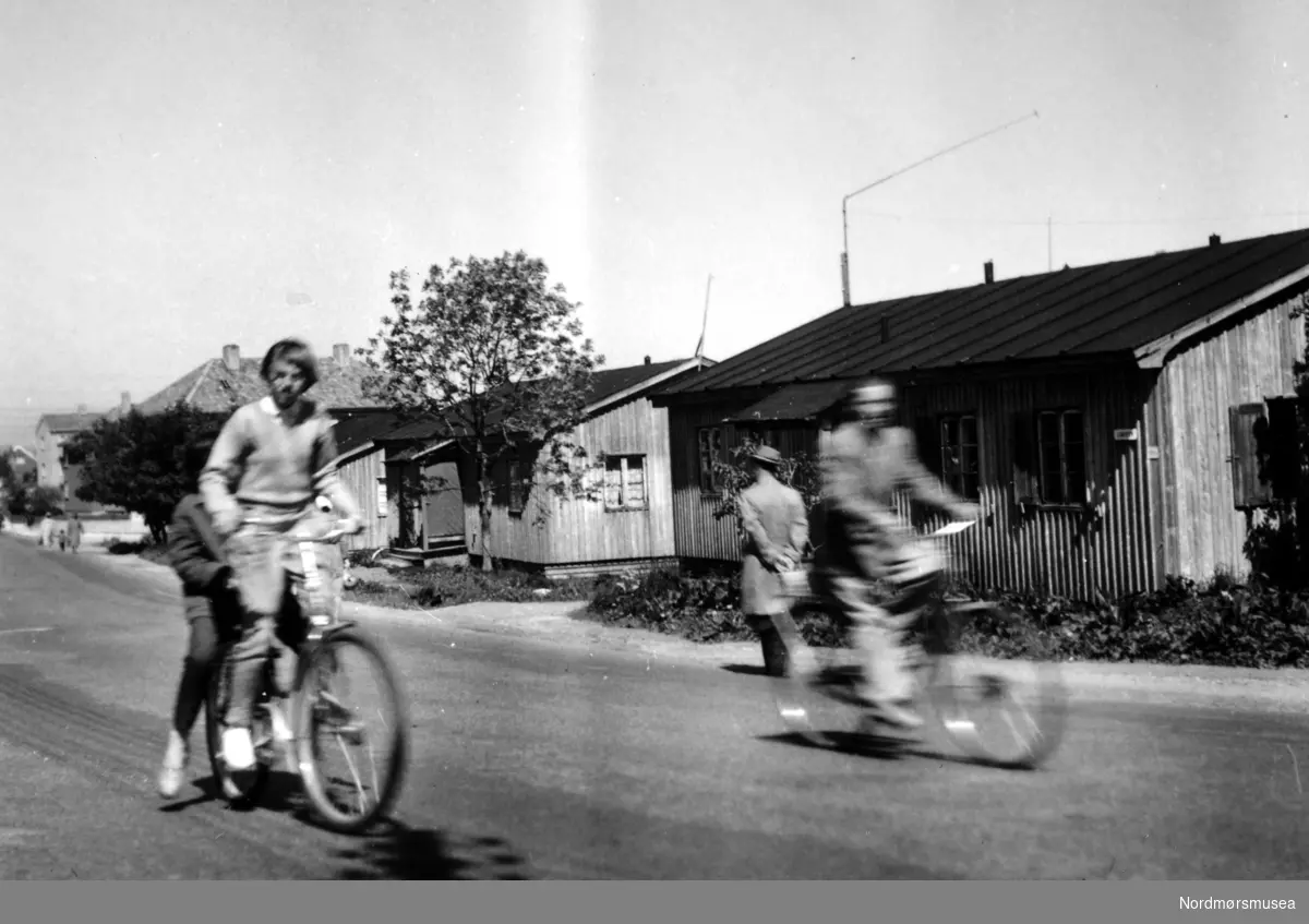 På bildet ser vi brakkene i Langveien, fotografert nær skillet ved Kaasbølsvei, med to syklister i forgrunnen. Bildet er datert 1958. Fra Nordmøre Museums fotosamlinger.
