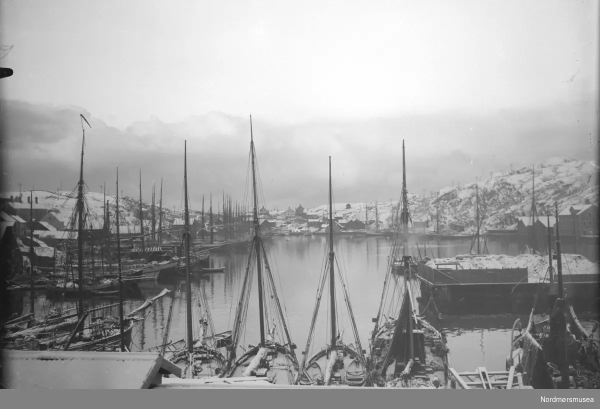 Foto av Vågen tatt fra Nervågen Verft (pr. 2009 Vedkaia/Gjestebrygga) i retning Øvervågen i Kristiansund. Vi ser båter i opplag, og til høyre ser vi kull lagret i hauger på Kranaskjæret. Fra Nordmøre museums fotosamlinger.
