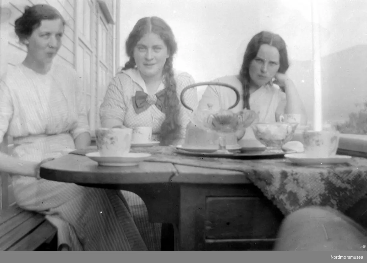 Tre kvinner rundt et tebord ute på trappen. Foto enten av familie eller slekt i Sverdrupfamilien, eventuelt fra deres bekjentskaper. Ukjent hvor, men trolig på Nordmøre eller i Romsdalen, Møre og Romsdal fylke. flette, te, kaffe, hår
 
Datering er trolig omkring 1920 til 1939. Fra Nordmøre museums fotosamlinger.
