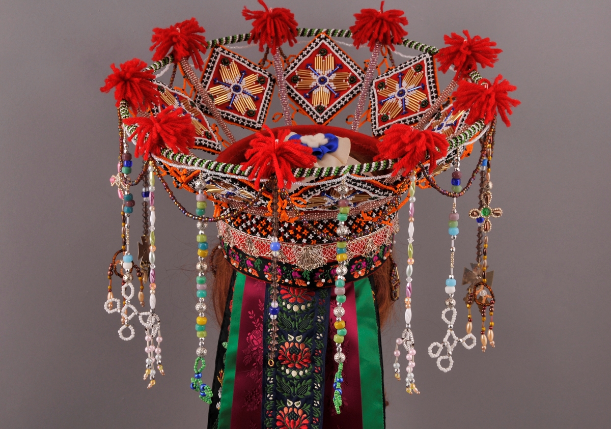 Brudekrone, nylaga.
"Pull" truleg med botn av stiv kartong og kledd med kraftig raudt klede. Påsydd (frå nedkant og oppover) eit band med satengbotn lansert blondemønster og påsydd kvite glasperler, ein sylvknipling og eit perlebendel. Perlebendelet er tredd med glasperler i svart, kvitt og orange.Sjølve krona er oppbygd rundt eit stativ av stål, raudlakkert. Heile stativet er dekt av glasperler i ulike fargar. Inni kvart "rom" er det eit sydd raudt kvadratisk klede som er pryda med glas- og stavperler av åttebladrose-mønster på begge sider, alle kvadrata er like og dei er montert på høgkant. I tillegg er det ein del ulike heng frå øvre kant av krona, her er det nytta ulike typer glasperler. På toppen av krona er det festa små duskar av laustvinna, raudt ullgarn i kvart skjæringspunkt. Inni krona, over hovudet, ligg eit ubleika band i kryss og i krysset er det sydd fast ein rosett.
Bak på krona er det sju heng av ulike band. På kvar side er det "øyrepynt". Frå sida og bakover er det 11 heng med ulike typer perler.