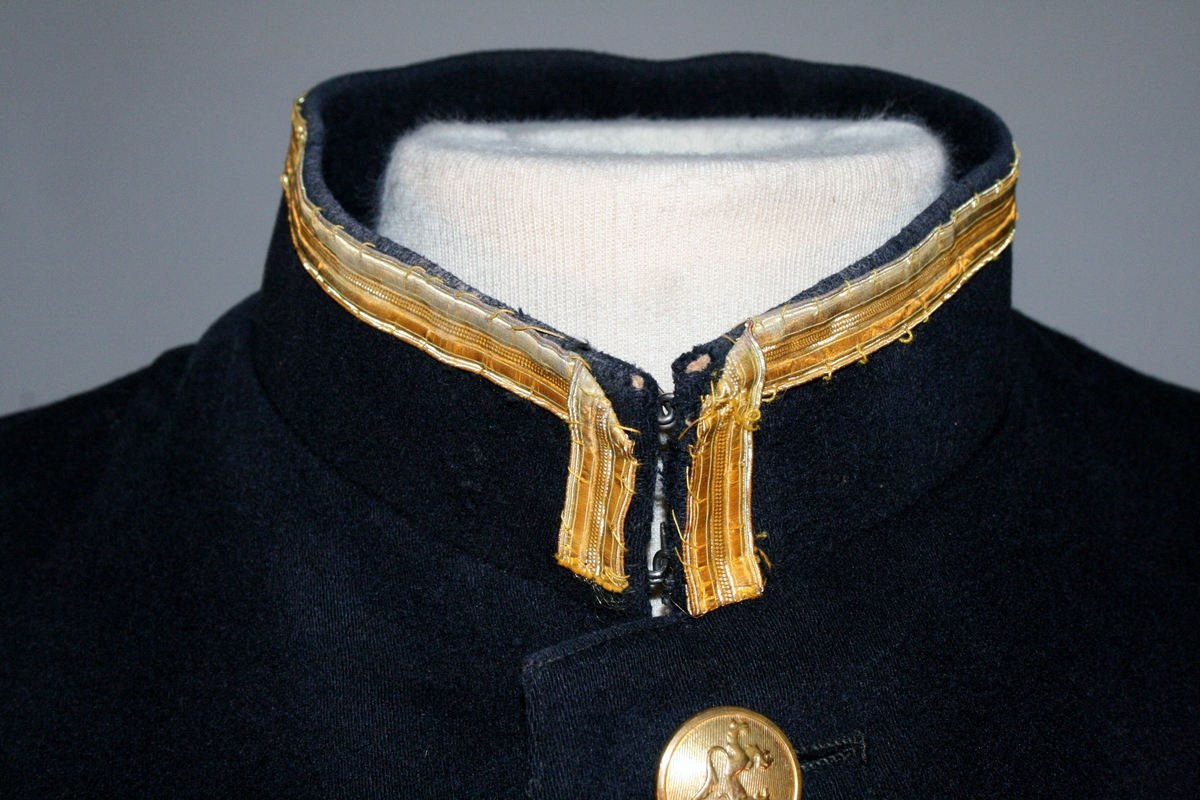 Uniformsjakke i sort med blåskjær med seks forgylte riksløveknapper. To brystlommer med klaff. Stående krage kantet med 12 mm gullbånd. Jakken er uten distinksjoner.