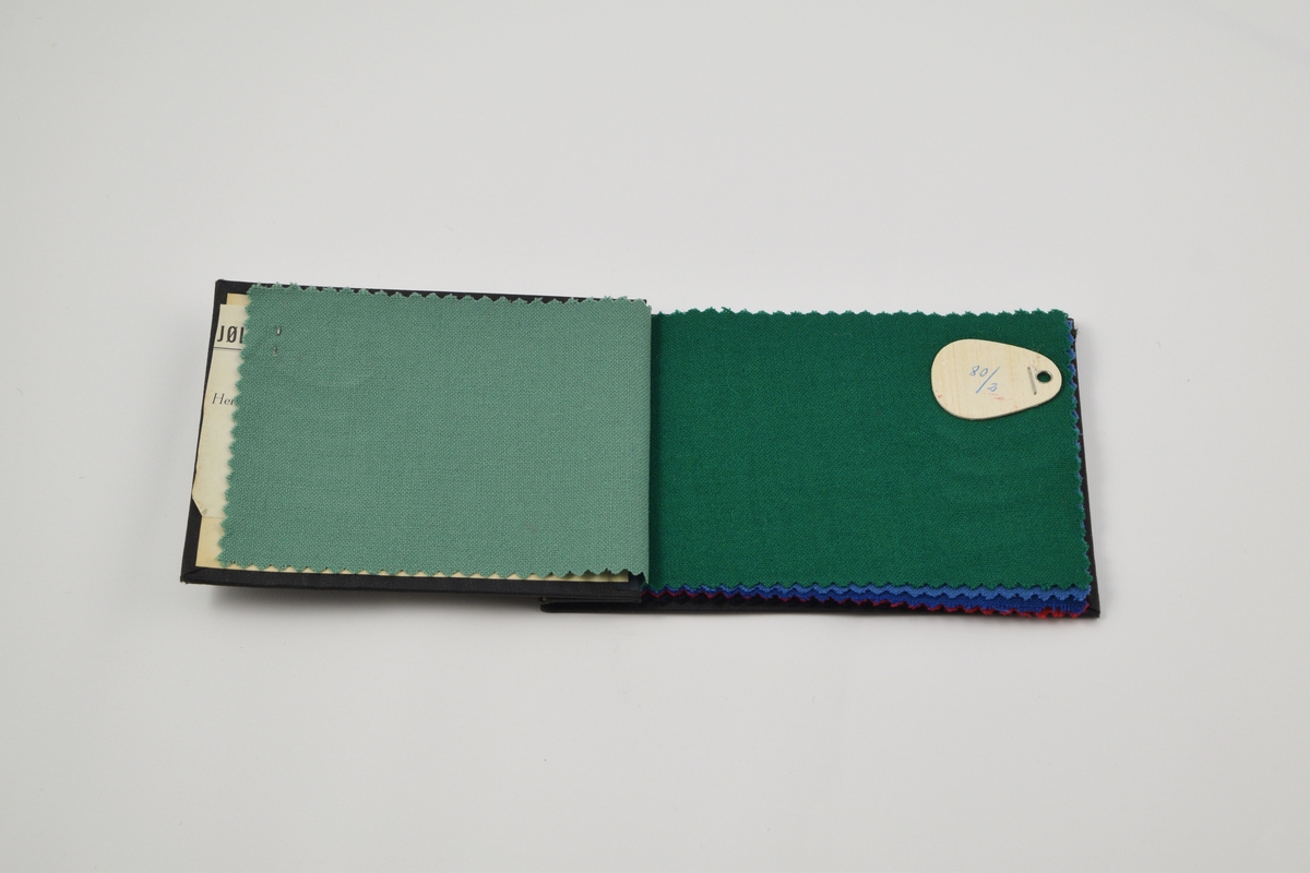 Prøvebok med 8 prøver. Tynne ensfargede stoff, toskaftvev.  Alle stoffer er merket med en dråpeformet tynn trefiner plate festet med metallstifter hvor nummer er påskrevet for hånd. På baksiden av merkelappene er det limt en papirlapp hvor det er trykket "NORSK FABRIKAT". 

Stoff nr. 80/1 (lys grønn), 80/2 (mørkere grønn), 80/3 (blå) 80/4 (mørkere blå), 80/5 (rød), 80/6 (brun), 80/7 (mørk blå). 80/8 (sort).