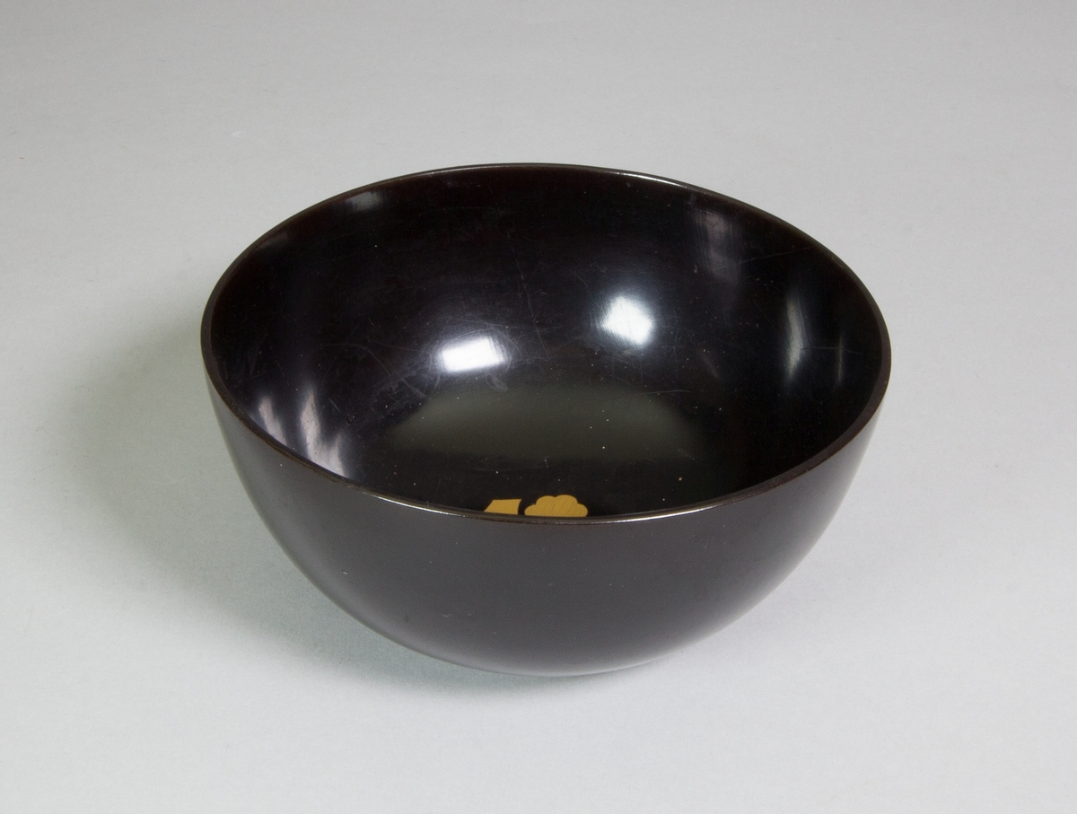 Skål, halvsfärisk, av svart lack. Invändigt inlagd guldfärgat blomliknande ornament.