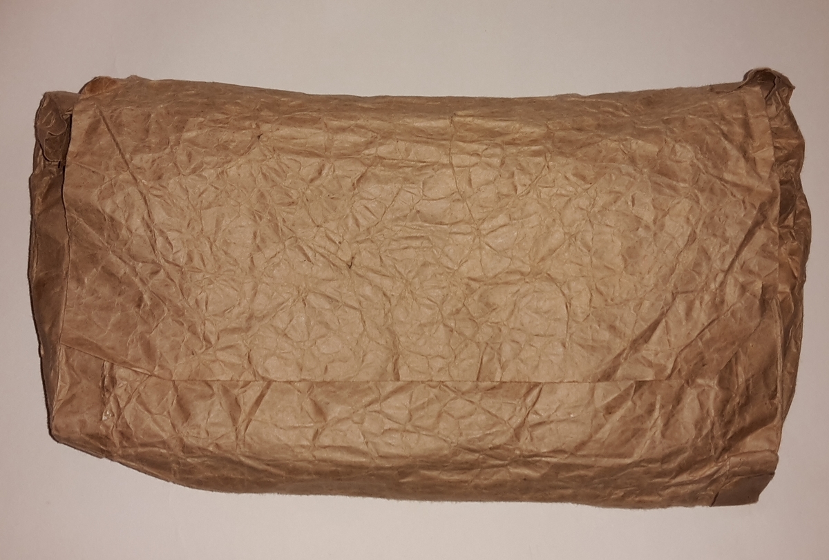 Iddisane ligg i papirpose laga av gråpapir, limt med limband i papir.