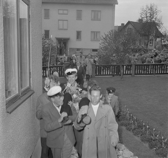 Studenterna andra dagen, 18/5 1954. 
En glad student bärs in i sitt hem. På gatan utanför passerar just ett annat studentfölje. 
Något suddigt foto.