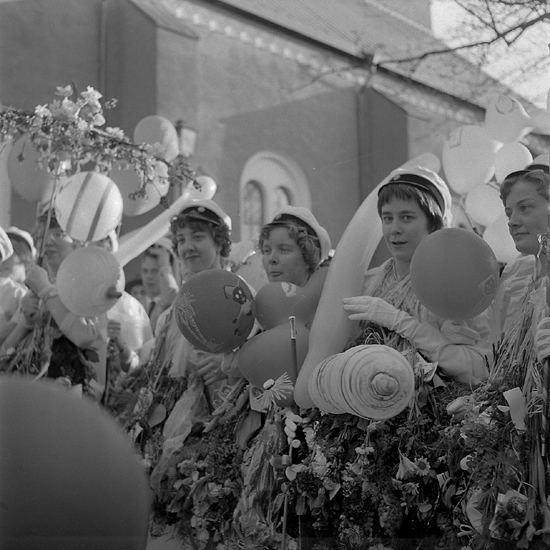 Studenterna, tredje d. 1960. 
Några kvinnliga studenter har samlats för att lyssna på talet vid Esaias Tegnérs staty. I bakgrunden skymtar domkyrkan. 
(Motljusfoto).