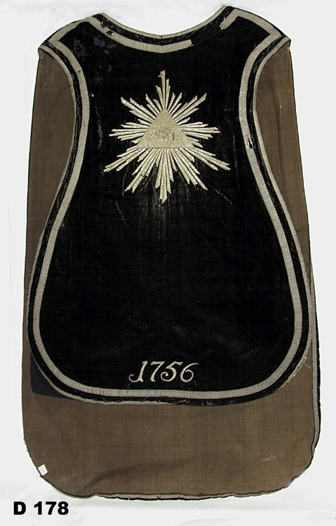 Mässhake av svart sammet, kantad med silvergaloner. På ryggsidan broderat krucifix i silver. Fodrad med grått linnetyg.
Daterad 1756.