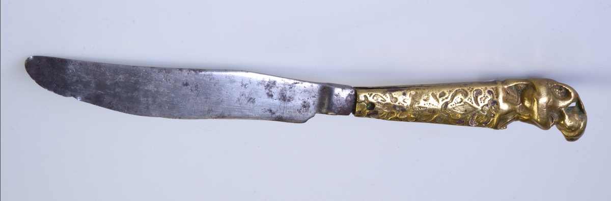 Kniv av jern med messingskaft som har mønster i metallet og øverst formst som en soldat med hjelm og som blåser i en sekkepipe.
