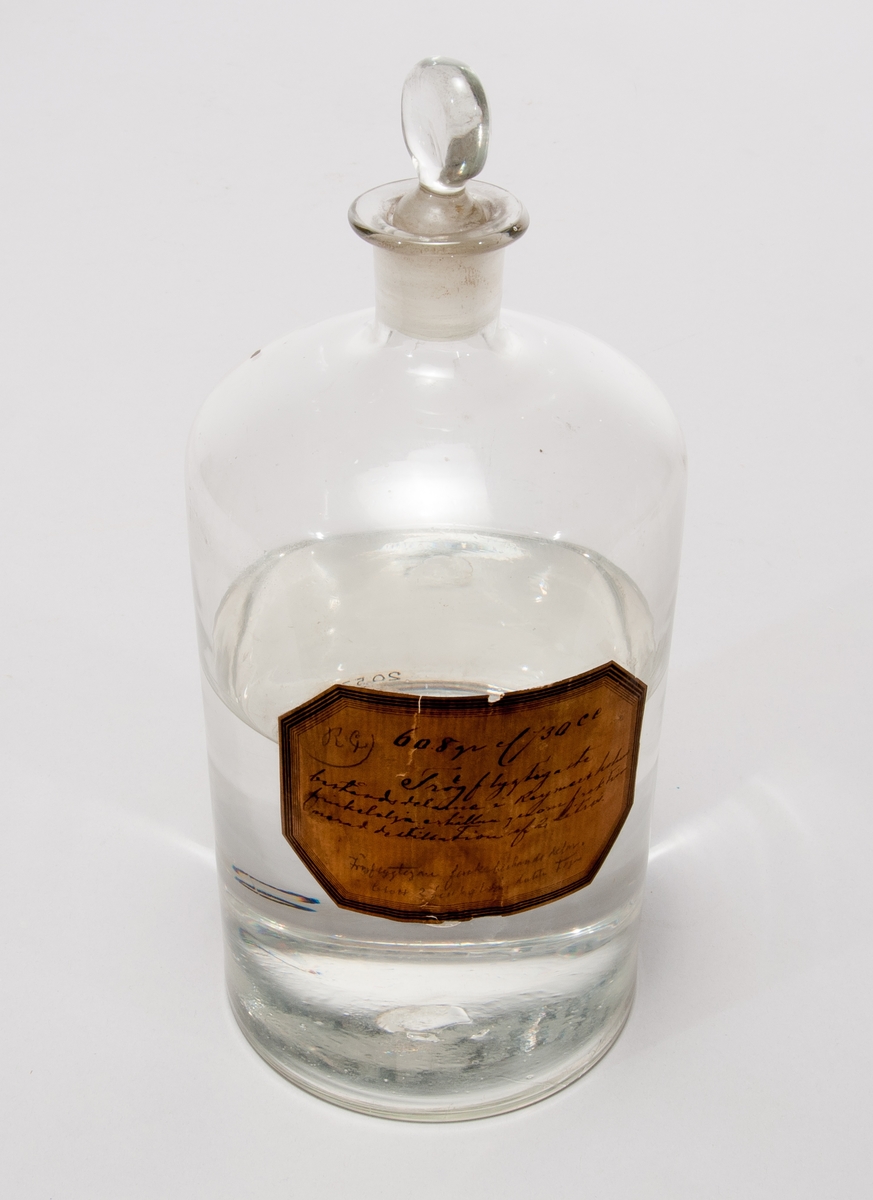 Finkelolja i  flaska av glas med etikett: "608 gr el 730 cc, Trögflyktigaste beståndsdelarne i Reymersholms finkelolja erhållna genom fraktionerad destillation af 2 liter."