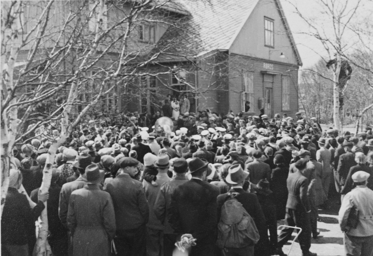 Fra mai-dagene 1945. Folkemengde samlet ved jernbanestasjonen, Røros. Midt i bildet sees deler av Røros janitsjarorkester