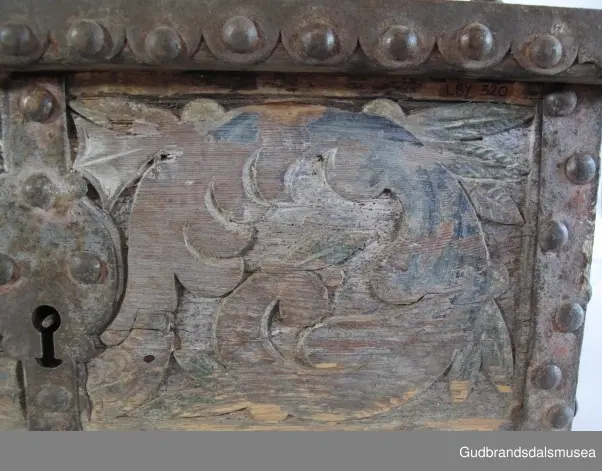 "Bladformer, smøygde band og drageornamentikk. Millom kantjarn og utskurden hev lokket fint utskorne små blad og halvrunde aggar. Vel vedlikehalde, sterk jarning og prydelege gangjarn. Truleg frå 1500 talet. Fra Haugen, Øystre Gausdal". (Jf. "Katalog for Lom Bygdesamling,1925).
Skrinrammen er holdt sammen av utvendige hjørnekantbeslag; jernhandtak i hver side. Fronten har nøkkelhullslås med beslag rundt. Lokket er satt samen av 2 bord, forsterket med jernbeslag rundt kanter på overside; to hengselbeslag festet til innside av lokk og bakstykke. Skrinsider blir holdt sammen av beslag ned langs hjørnekanter; har jernhandtak festet på jernbeslag.
Bunnen er satt sammen av 2 bord, festet til hverandre med to forsenka treplugger; bunnen var opprinnelig festet til underkant av skrinsider med 4 x 4 trenagler,seinere festet med spiker. 
Det er jernbeslag  på bakstykket midt, rundt hjørnekanter, omkring nøkkelhullslås, rundt lokk samt 2 handtak med beslag. Alle beslag er festet med store jernnagler; beslag på sidestykker er festet med små jernnagler under skrinbunnen. 3 av 8 bunnfester for beslag er fortsatt intakte.
DEKOR. De store jernnaglene med forskjøvet plassering på beslag ble sannsynligvis brukt som dekorelement; runde beslag på sider, bakstykke og front. Flatskurd på lokk med flettet, stilisert renessanseranke, der bladverk er "omgjort" til småspiraler eller rundinger.  På skrinsidene akantusskurd med c-former, bladtunger uten stilk og naturalistiske småblad i rokokkostil. Flatskurd var vanlig i Gudbrandsdalen i perioden ca. 1650-1750, mens akantusmotivet først ble vanlig på bruksgjenstander i løpet av siste halvdel av 1700-tallet. Den mørkere grønne og blå dekorfargen var vanlig i siste del på 1700-tallet; den brune bunnfargen var vanlig i bruk fra 1780-tallet. 
BRUK. Før kofferten kom i bruk hadde man reiseskrinet, som ble brukt til oppbevaring av bl.a. klær, verdisaker og mat på reiser. Skrinet hadde ofte et eller to mindre, smale rom langs den ene skrinsiden og ett større rom. De fleste reiseskrin var i tillegg forsterket med jernbeslag langs alle kanter og med en solid nøkkelhullås til sikring mot støt, slag og tyveri.