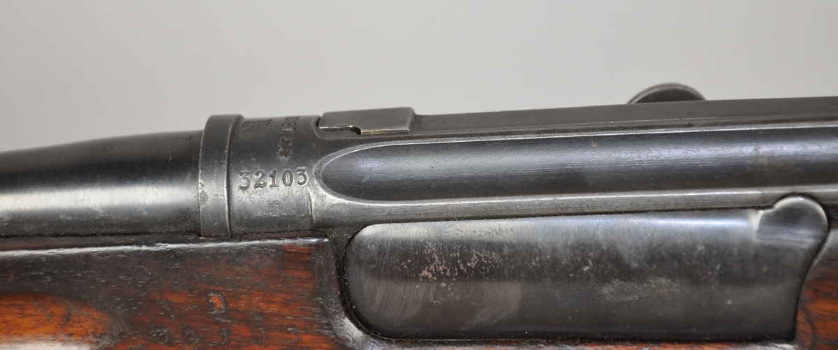 Krag-Jørgensen gevær mørkebrun kolbe og forskjefte av tre. Geværet har grønn stoffreim.