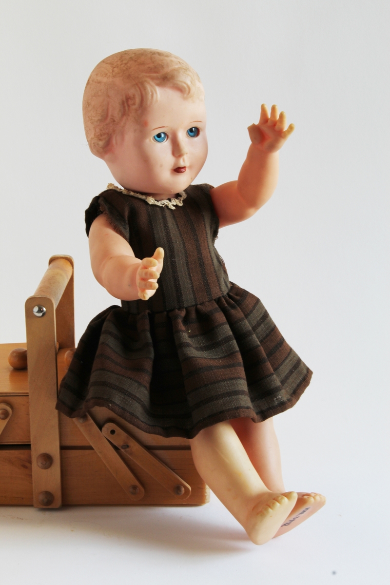 Gitt av Gerd Berit Lie. 
Dukken har knall blå øyne og røde lepper. Eier beskriver dukken som en "baby-dukke". Dukken ble vunnet på basar av moren til Gerd Berit, Elise, i ca 1960/61. Moren vant denne dukken samt en en annen dukke (KMR.3438).