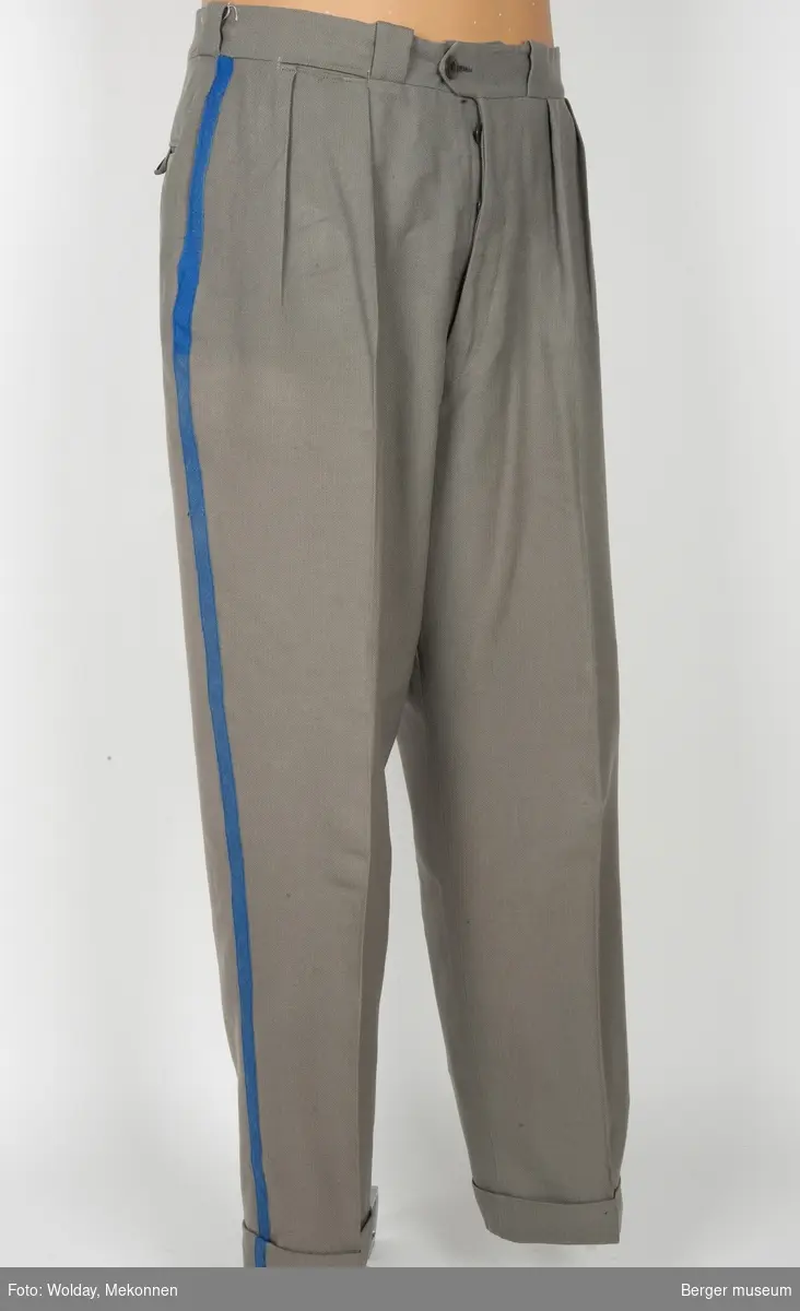 Buksene er grå med en kornblå stripe nedover fra linningen fra begge sider. Buksene har sidelommer, baklomme og en liten lomme foran. Linningen er foret. Det er brodert TH i linningen bak, antagelig initialene til brukeren av buksa. 