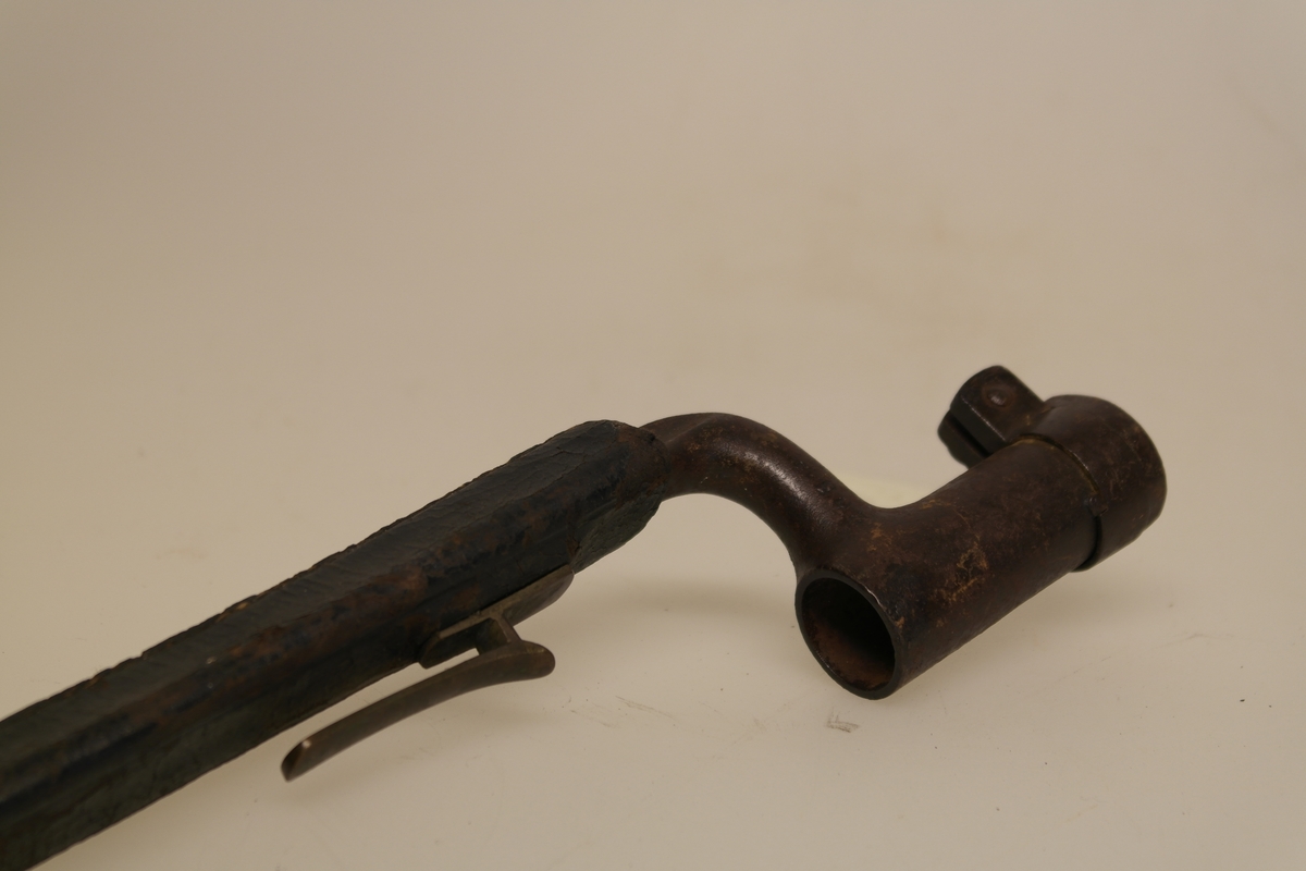 Stålbajonett med slire. Bajonetten er støpt. Sort lærslire med messingdupp og hempe. Sliret er sydd,  påmontert støpt messingfeste.