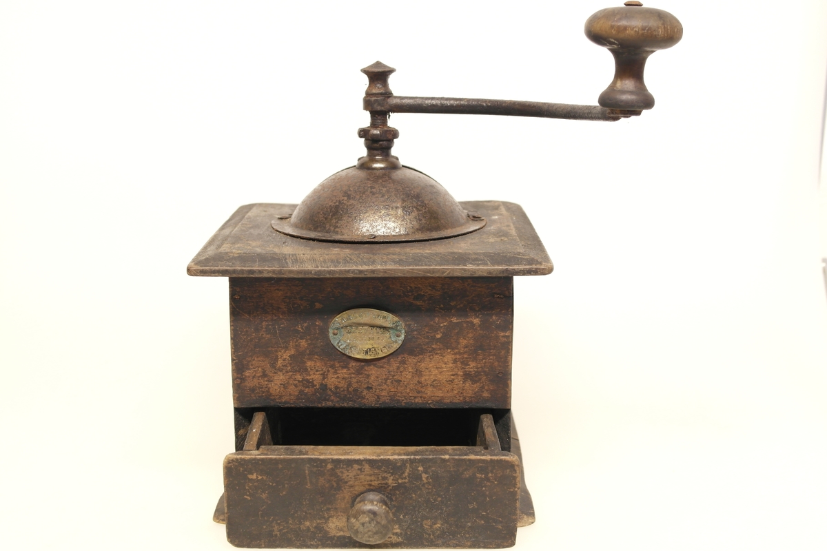 Kaffekvern (a og b) i tre, jern og messing. 
a) Kvadratisk kasse med topplate og bunnplate. Sveiv som går ned til innsatt tannhjul, som kverner kaffebønnene. Klokkeformet deksel som kan åpnes med en klaff som skyves til siden. Messingskilt med stempel.
b) Skuff som samler opp den malte kaffen. Stiftet i hjørner og bunnplate.