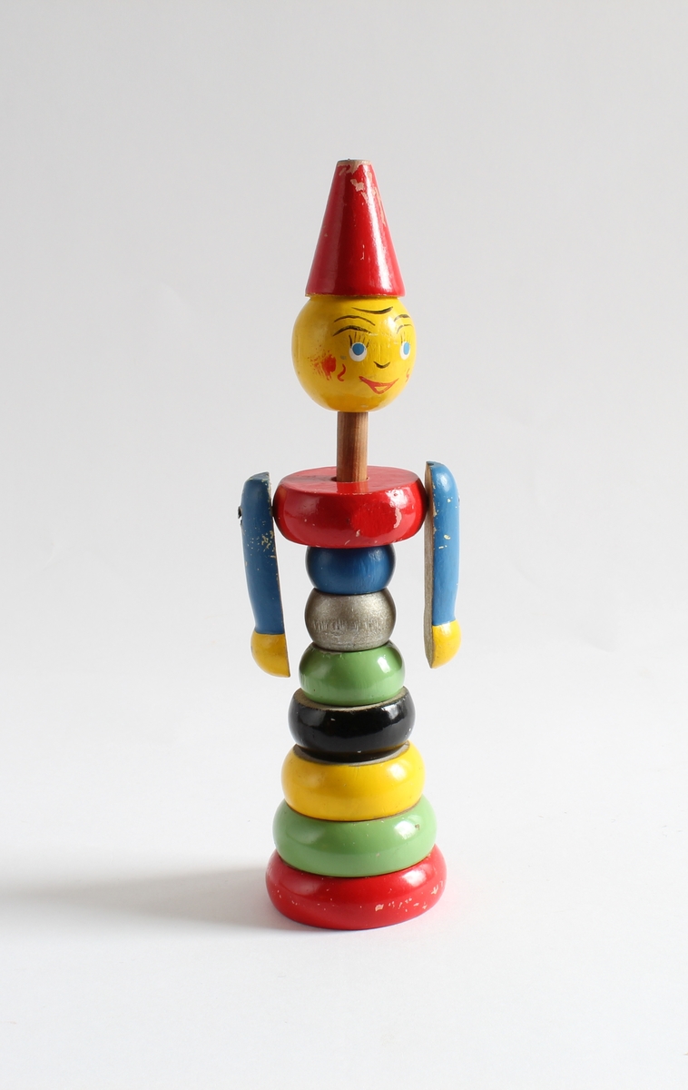 Giver/tidligere eier, Gerd Berit Lie (f. 01.11.1954). 
Det er en "putte på figur" til småbarn. Så de kan putte treklosser på en pinne, og når den pinnen er fylt opp ser det ut som en sprellemann. Klossene er i Brio-farger, rød, grønn, blå, gul og svart.  Ca 20 cm høy. Det er påtegnet et smilende ansikt på figuren og bærer en rød hatt. 

Giver/tidligere eier, Gerd Berit Lie (f. 01.11.1954). Gerd Berit er enebarn. Hun var etterlengtet og foreldrene var godt voksne da hun ble født. Mor var 44 år og far 45. Både moren og faren laget mange leker og utstyr til dukkene til Gerd Berit. Familien bodde i en drabantby i Oslo, men faren var fra Fulu i Sør-Odal. Farens brndomshjem var familiens feriested i alle år. Gerd Berit Lie hadde flyttet til Kongsvinger da hun ga samlingen til Kvinnemuseet.