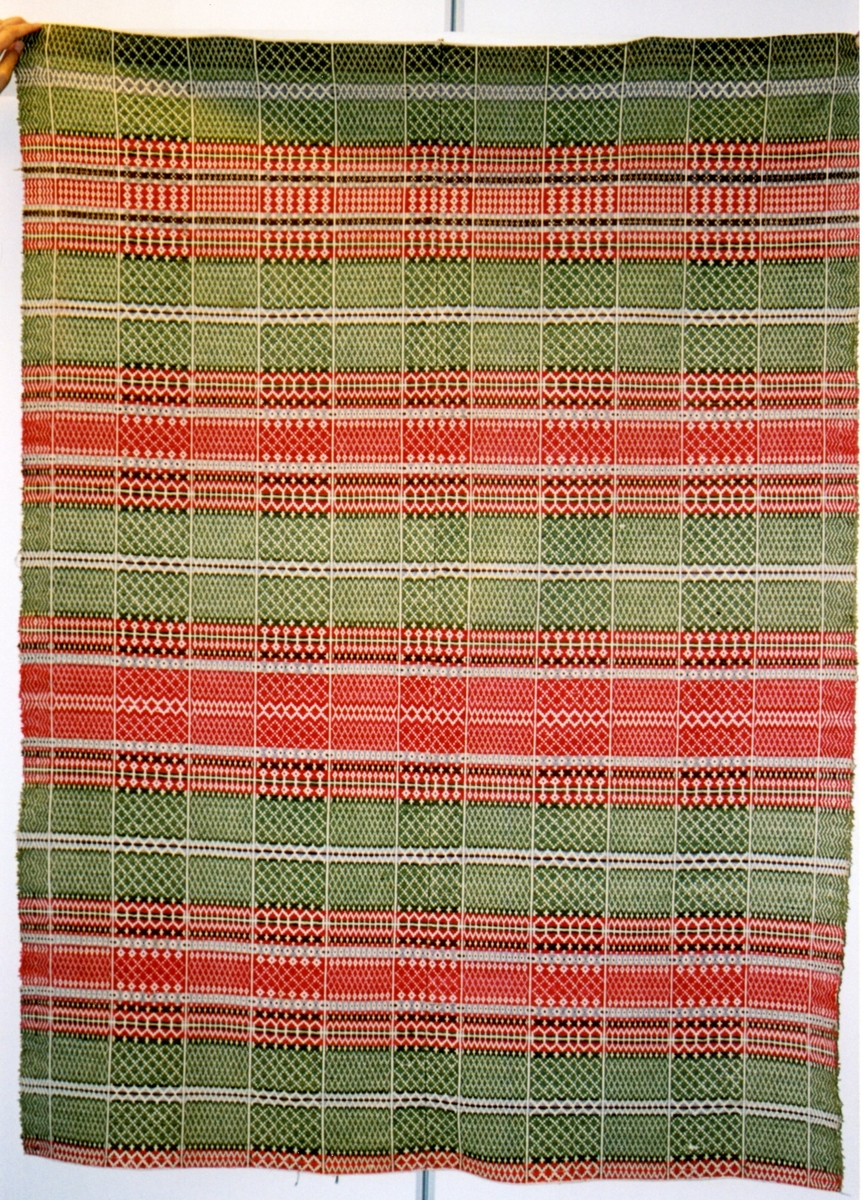 Det er ruter i rødt, grønt og beige, ca 20 x 202,5 cm. I rutene er det vevd inn mønster med farger i to forskjellige varianter.