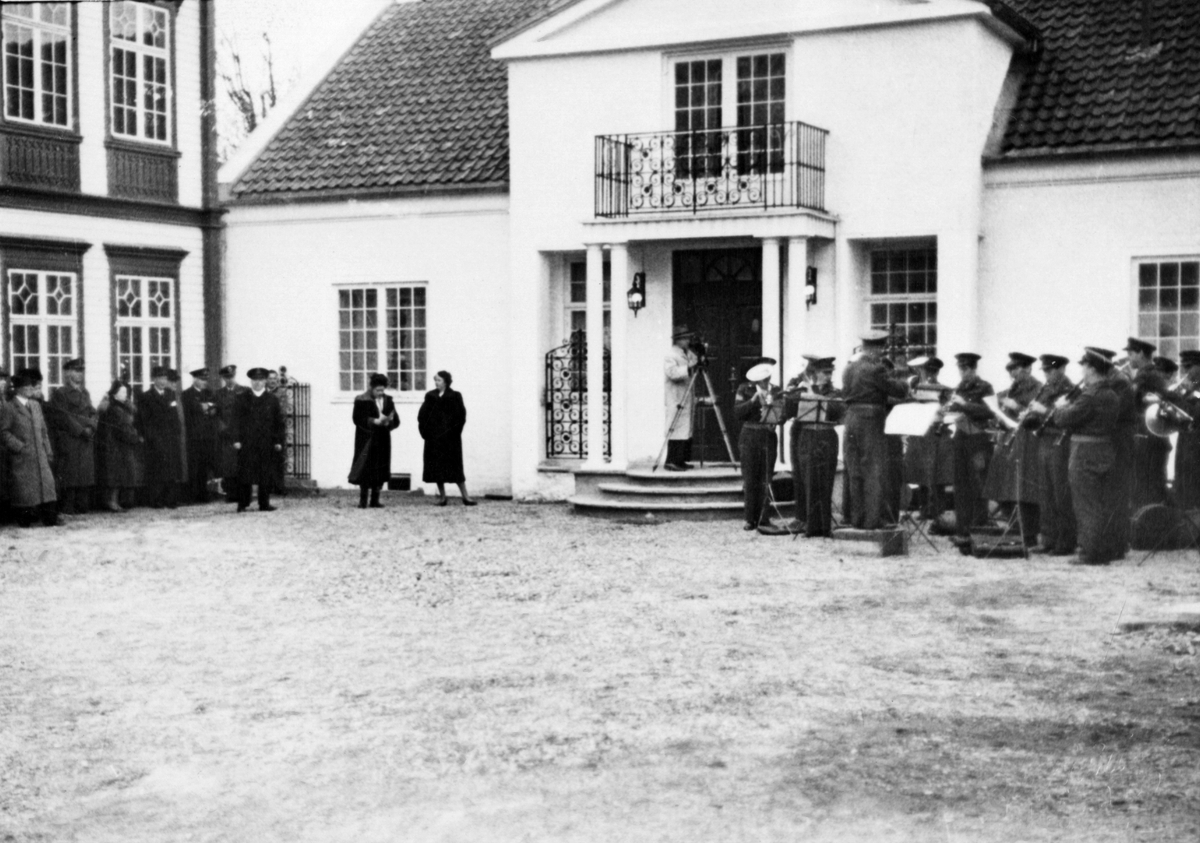 Bilde av den offisielle åpningen av Tordenskioldmuseet. Victoria Bachke står til venstre foran direktørboligen, og forsvarets distriktmusikk-korps står til høyre. På trappen står det en fotograf.