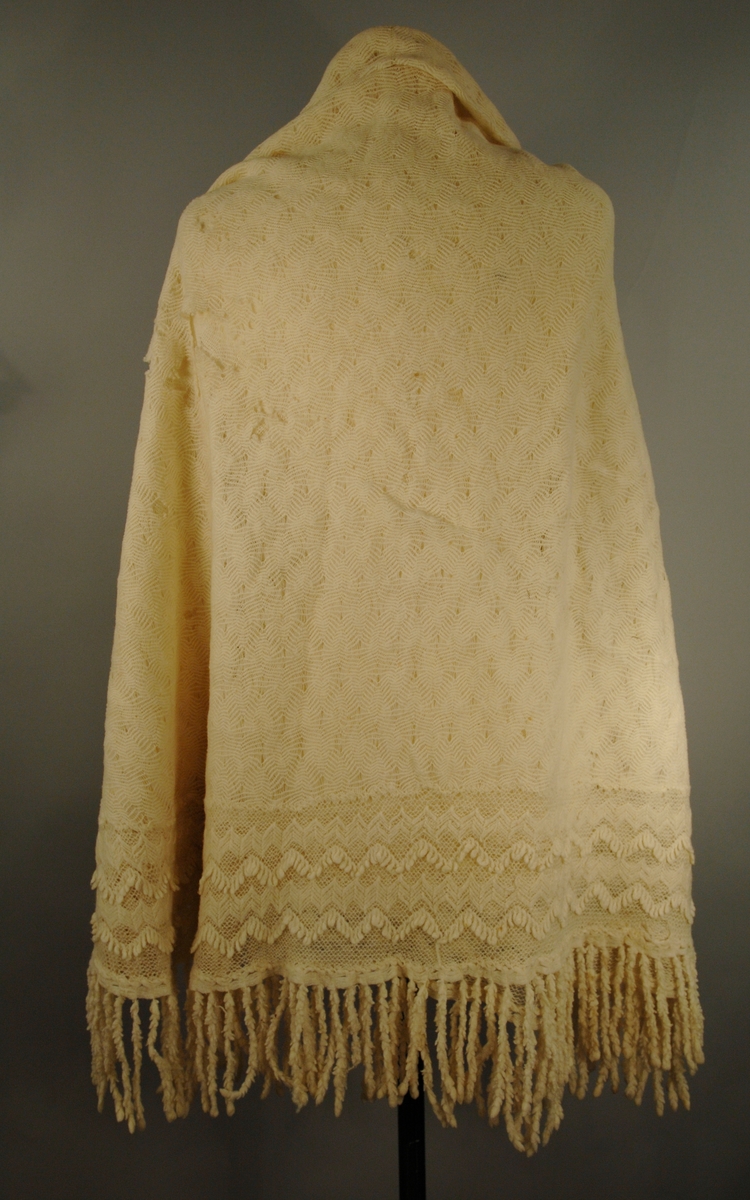 Strikket i tynn ulltråd. Den innerste firkanten er strikket i eit stykke. Knaten rundt påsydd slik at hjørnsne blir avrunda. Dersetter er det påsydd frynser med symaskin.