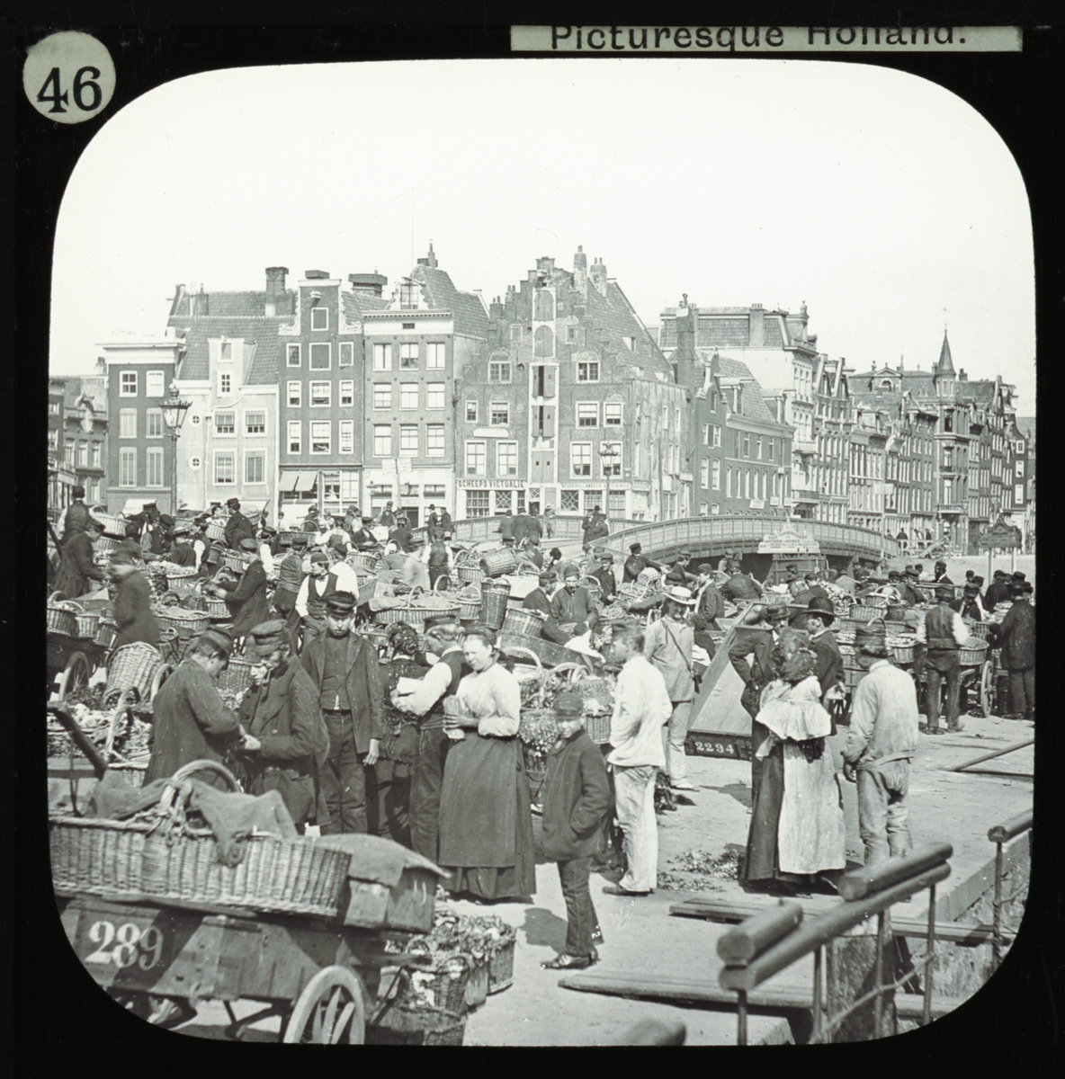 Amsterdam - the Vegetable Market. Bilden visar en ekonomisk kommers och rörelse, med en kanalbro och Amsterdams karakteristiska hus i bakgrunden.
Ur serien "Pictueesque Holland".