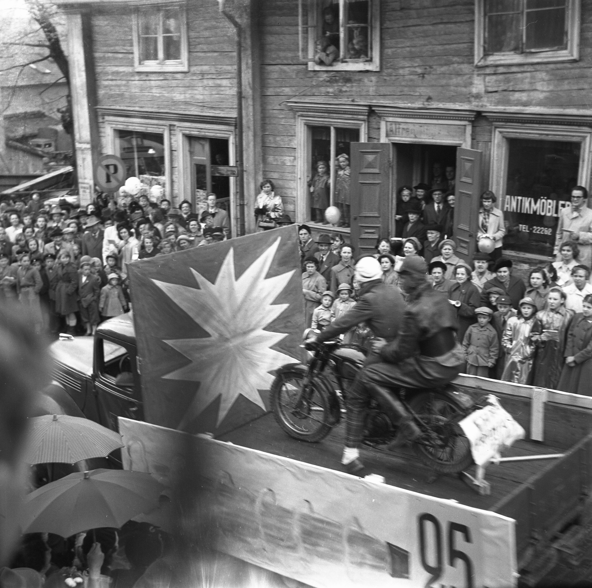Orig. text: Majkarnevalen 1952.

Majgubbar på en motorcykel på ett lastbilsflak. Storgatan.