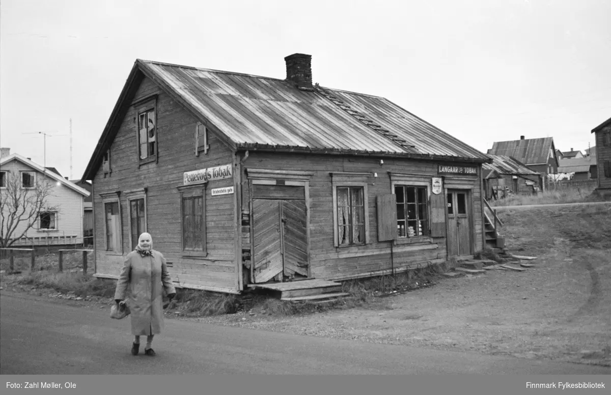 Vadsø, oktober 1969. Gammelt butikklokale med originale butikkskilt. Kvinne i forgrunnen.