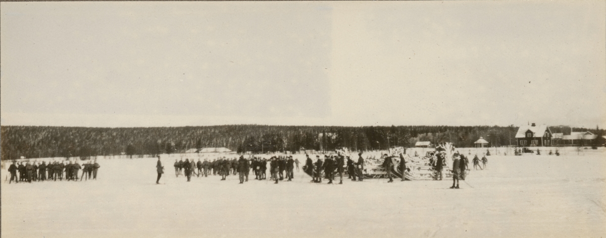 Tre stridsvagnar med vinterkamouflage på äng med soldater samlade omkring.