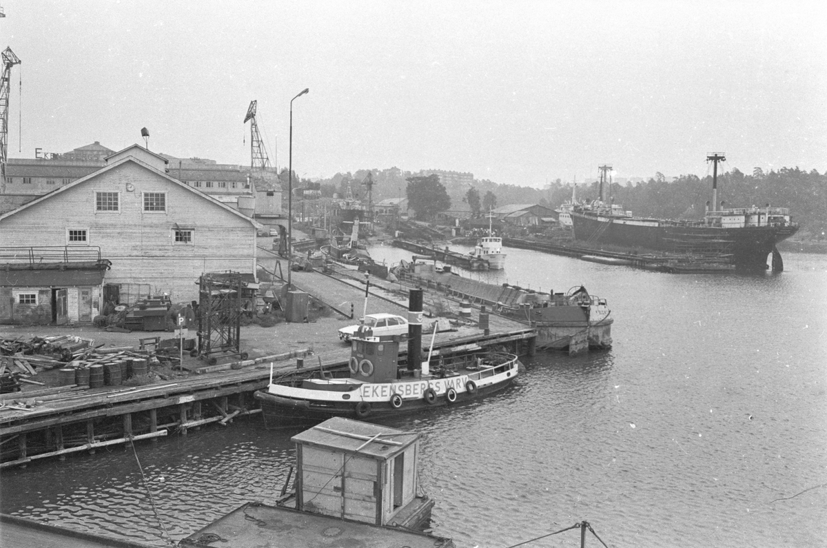 Ekensbergs varv 1970. Varvsområdet sett mot öster, med Mörtviken till höger. I förgrunden bogserbåten EKENSBERGS VARV (1891, urspr. WIDAR), bakom denna oidentifierad pråm från Skånska Cementgjuteriet ("SGC"). I bakgrunden kan urskiljas bogserbåten BRAGE (urspr. LINGARÖ) och pråmen MONARK (urspr. lastångfartyget MASILIA).