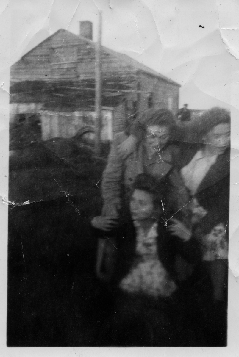 Ruth Kandola og venninner i Golnes i trivelig lag. Den ene blir båret på ryggen. I bakgrunnen ses en mannsskikkelse ved siden av bolighus.