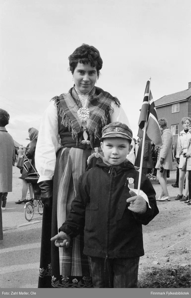 17.mai i Vadsø 1969. Fotografert av Ole Zahl Mölö. Kvinnen er kledd i Nordlandsbunad og gutten holder et norsk flagg. Lua er matrosinspirert med anker og gullsnor.